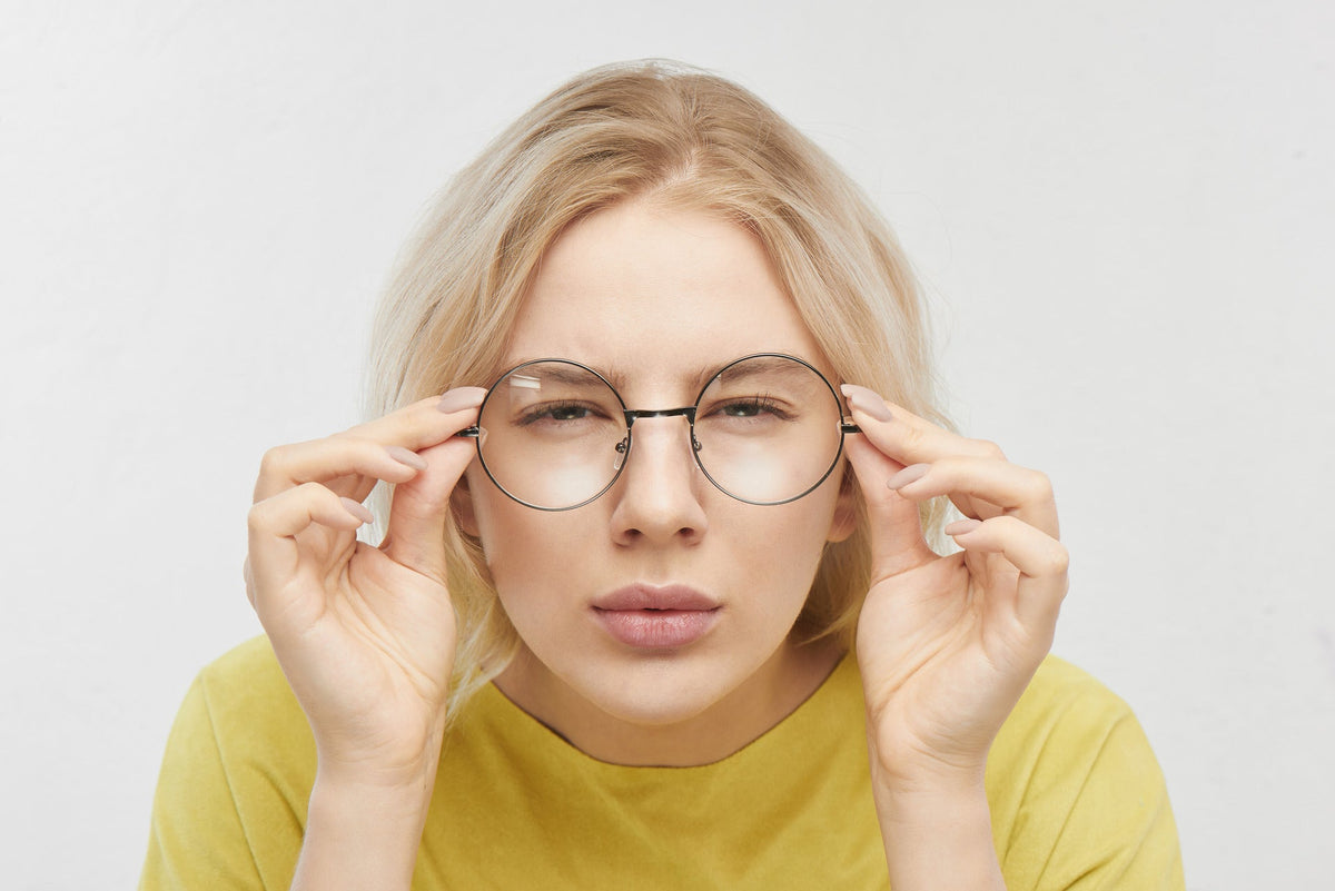 Mujer entrecerrando los ojos ajustando sus gafas redondas