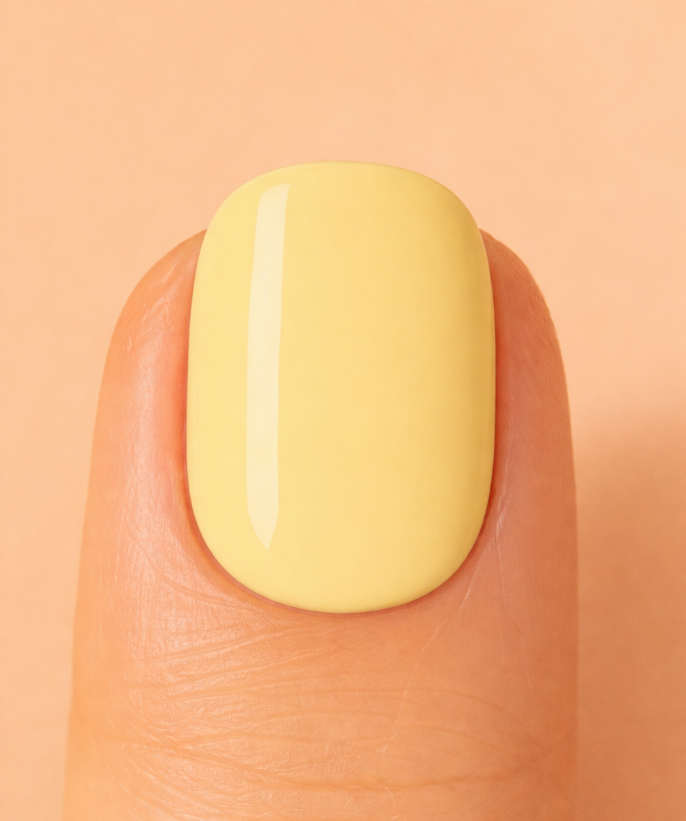 Yellow nail polish on a finger nail against a peach background