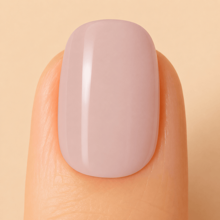 A close-up of a fingernail with a smooth, glossy, dusty mauve manicure against a solid beige background.