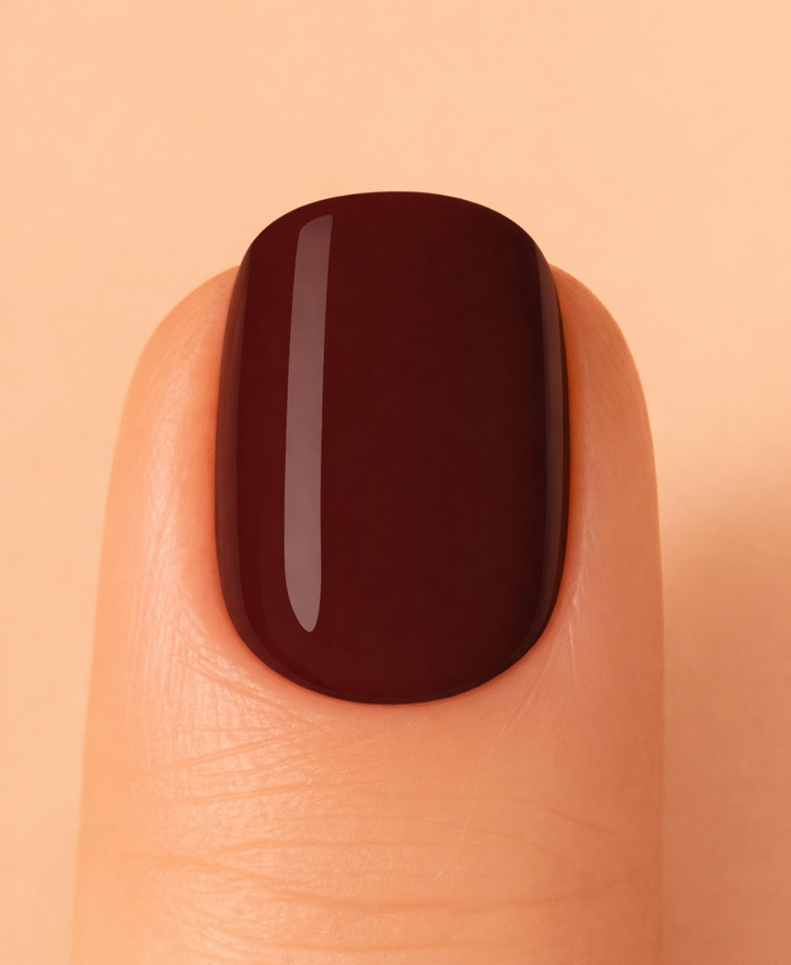 Nail with dark cherry polish on a beige background